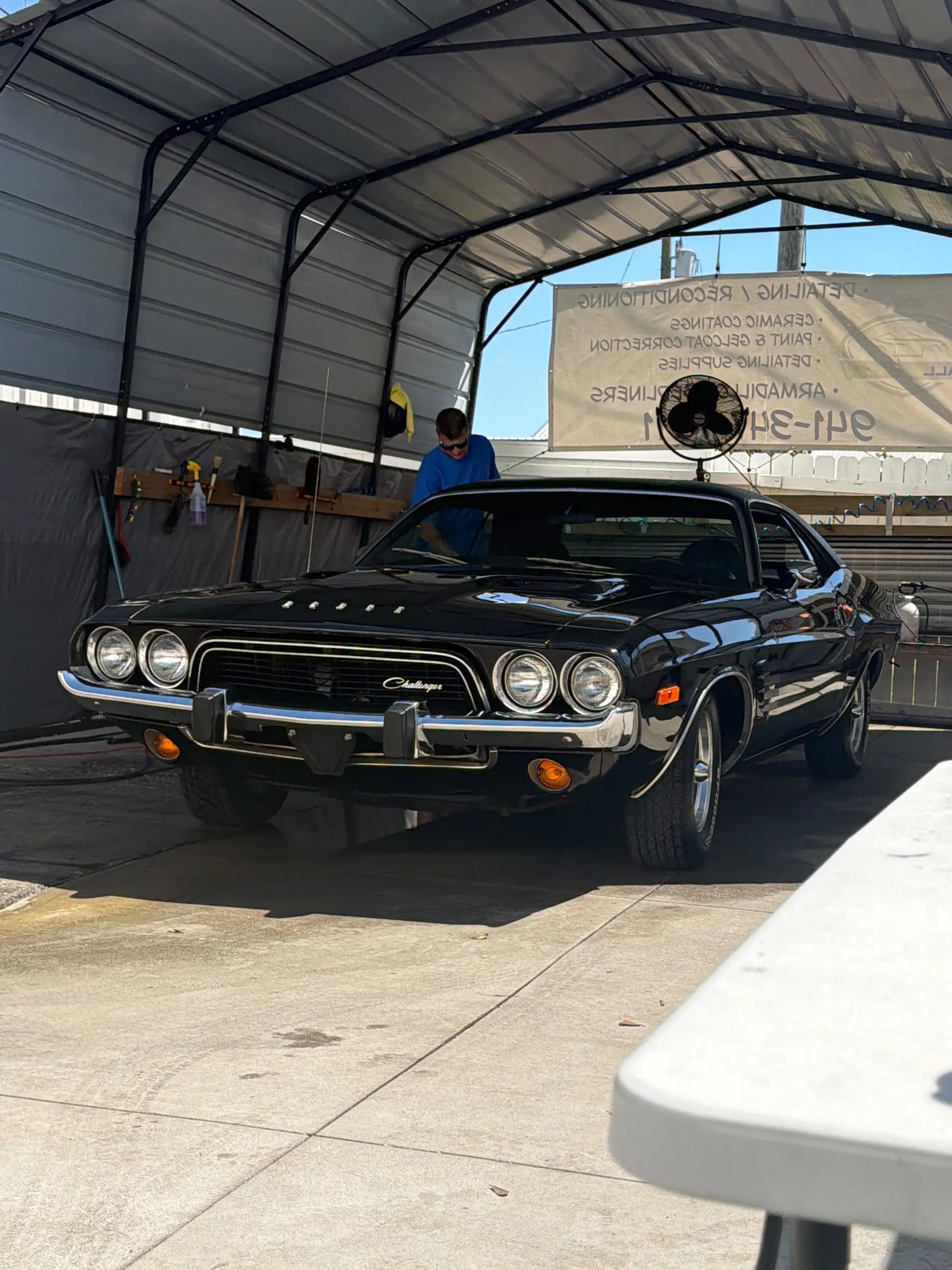 Glossy black Dodge Challenger being detailed under the shop canopy.